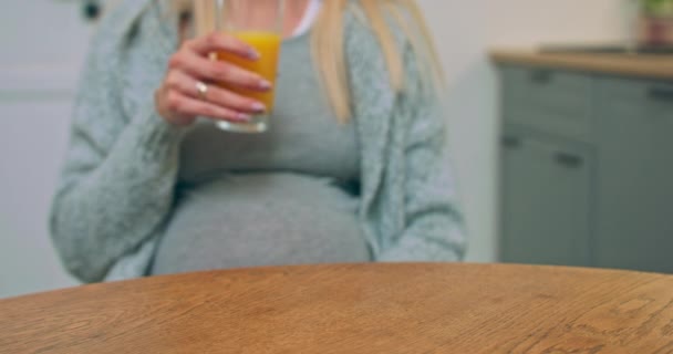 Mujer embarazada bien parecido sentado en la mesa de la cocina soñando, bebiendo un jugo y acariciando — Vídeo de stock