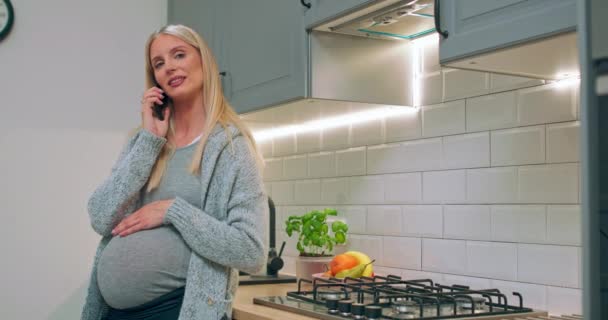 Jovem mulher grávida feliz falando no telefone celular com o marido na cozinha — Vídeo de Stock