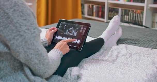 Video van mooie jonge zwangere vrouw op zoek echografie van haar baby op digitale tablet, terwijl — Stockvideo