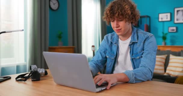 En ung tonåring studerar med en laptop i vardagsrummet. Snygg man som pratar med — Stockvideo