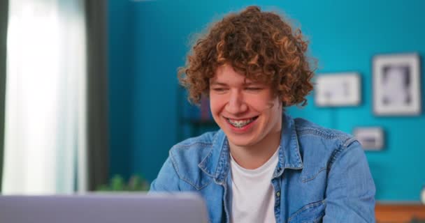 Молодой подросток учится с ноутбуком в уютной гостиной. Красавчик болтает — стоковое видео
