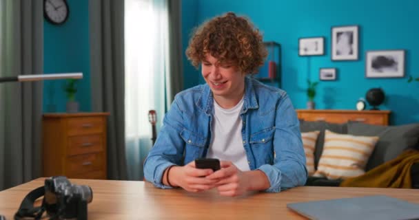 Портрет белого подростка с вьющимися волосами в уютной гостиной с помощью смартфона — стоковое видео