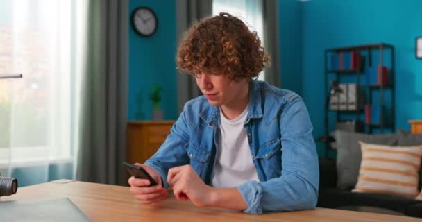 Portrét kavkazského dospívajícího chlapce s kudrnatými vlasy v útulném obývacím pokoji pomocí chytrého telefonu — Stock video