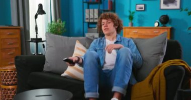 Genç bir adam apartmanın oturma odasına girer, kanepeye oturur, döner.