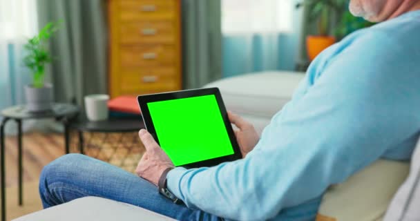 Homem velho adulto em casa usa verde Mock-up Screen Tablet. Ele está sentado em um — Vídeo de Stock