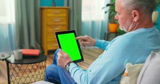 Senior Man thuis gebruikt Green Mock-up Screen Tablet. Hij zit op een bank. — Stockvideo