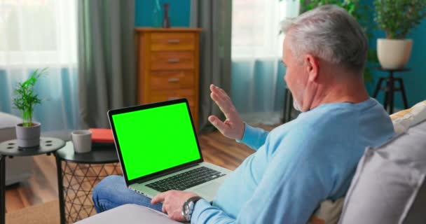 Mann benutzt Laptop mit grünem Bildschirm, der zu Hause auf einer Couch sitzt. Ein — Stockvideo
