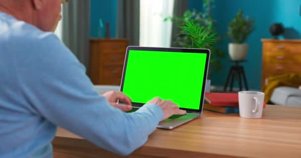Primer plano de un hombre utiliza el ordenador portátil con pantalla verde simulada mientras está sentado en el escritorio — Vídeos de Stock