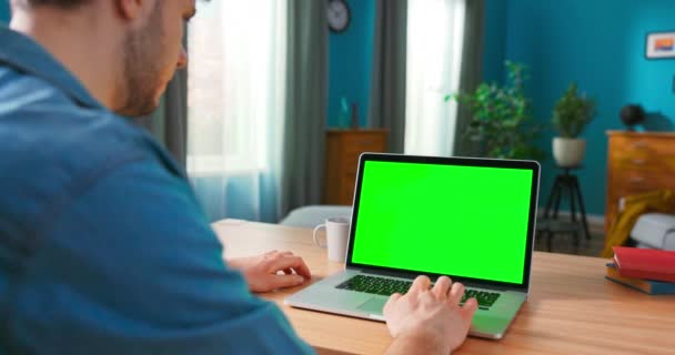 Homem usa laptop com tela de Mock-up verde enquanto sentado na mesa em seu aconchegante — Vídeo de Stock