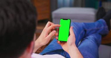 Evdeki genç adam yeşil ekran akıllı telefonu kullanıyor. O yalan söylüyor.