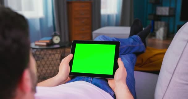 Ung man hemma Lägga på en soffa Använda med grön Mock-up Screen Tablet Computer. — Stockvideo