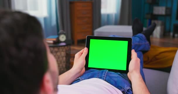Hombre joven en casa Descansando en un sofá usando con Green Mock-up Screen Tablet Computer — Vídeo de stock