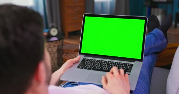 男人躺在沙发上，在绿色模拟屏幕笔记本电脑上工作。盖伊 — 图库视频影像