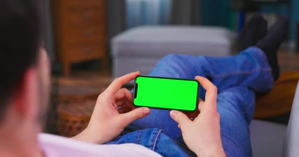 Étudiant garçon se repose sur un canapé en utilisant avec Green Mock-up écran téléphone cellulaire dans — Video