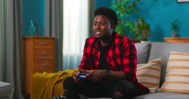 Een gefocuste jonge gamer zit op een bank en het spelen van video games op een — Stockvideo