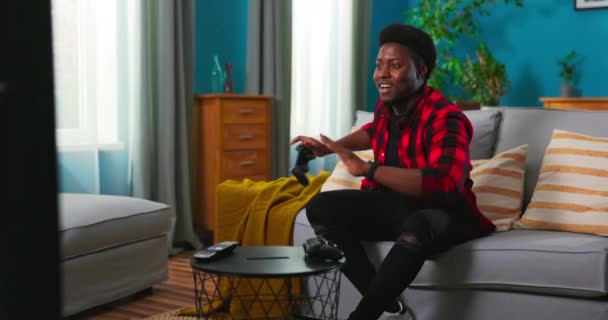 Zwarte Afro-Amerikaanse opgewonden man zittend op een bank, met een joystick videospelletjes spelend, voelen — Stockvideo
