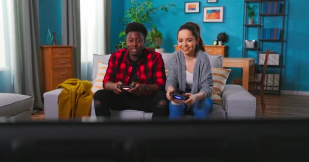 Αφροαμερικάνοι ευτυχισμένοι νέοι παντρεμένοι παίζουν βιντεοπαιχνίδια καθισμένοι στον καναπέ στο σπίτι. Όμορφος. — Αρχείο Βίντεο