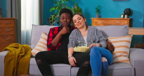 Wesoła Młoda para śmieje się i rozmawia oglądając telewizję razem na kanapie w domu — Wideo stockowe