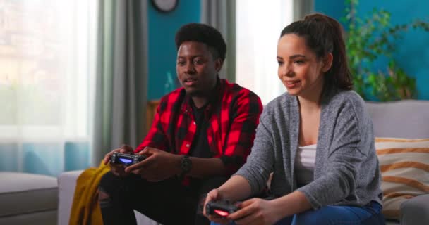 행복 한 젊은 다국적 부부가 소파에 앉아 콘솔에서 비디오 게임을 하는 모습. — 비디오