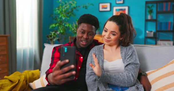 Homme et femme font un appel vidéo, prenant selfie assis sur un canapé ensemble à la maison. — Video