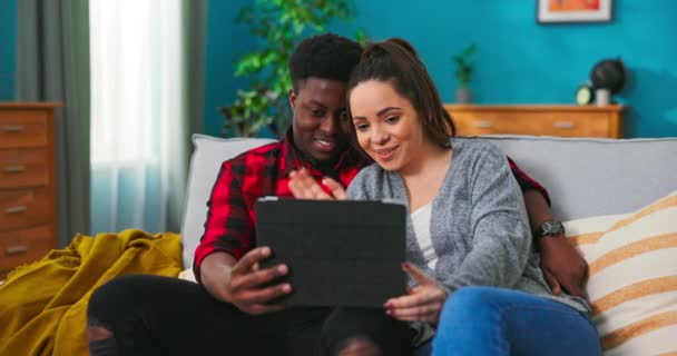 Multietnický americký pěkný mladý pár sedí na šedém gauči v útulném pokoji, zatímco — Stock video