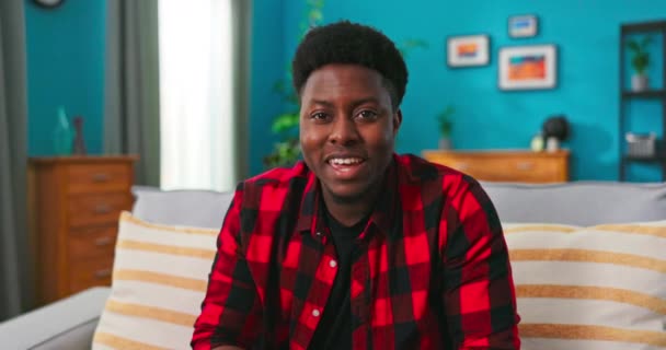 Um estudante afro-americano bonito se senta no sofá em uma sala de estar e hospeda — Vídeo de Stock