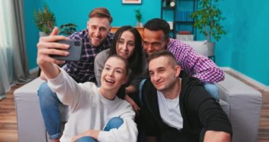 Neşeli, çok ırklı bir arkadaş grubu birlikte kanepede oturup akıllı telefonla selfie çekiyorlar.