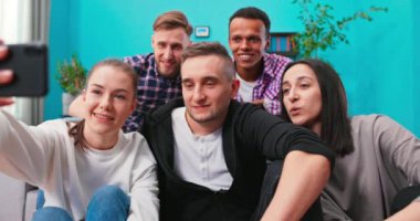 Neşeli, çok ırklı bir arkadaş grubu birlikte kanepede oturup akıllı telefonla selfie çekiyorlar.