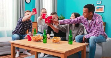 Arkadaşlığımızı kutlamak için kadeh kaldıran bir grup arkadaş masada oturmuş içki içiyorlar.