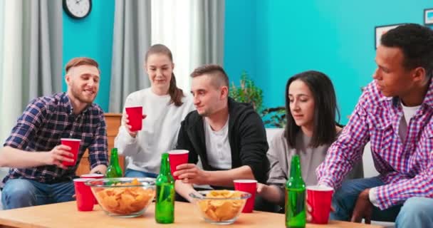 Grupo de jóvenes amigos alegres multiétnicos viendo partidos deportivos en la televisión mientras se sientan juntos en — Vídeos de Stock