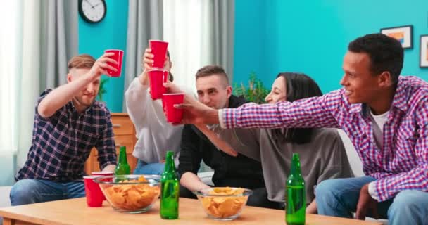 多国籍の友人は、小さなホームパーティー、会議、ソファに座って、ビールの赤いカップをクリックしている, — ストック動画