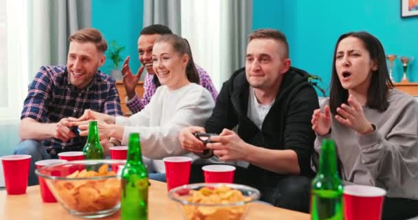 Multinationale Freunde sitzen zu Hause auf der Couch und spielen Videospiele auf der Konsole. Fröhlich gemischt — Stockvideo