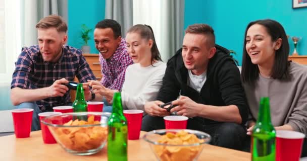 Un grupo multinacional de estudiantes universitarios se sientan en el sofá y juegan a videojuegos en — Vídeos de Stock
