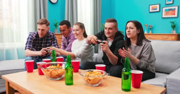 Fröhlich gemischte Rassen Freunde ruhen im Zimmer sitzen auf sfoa Videospiele spielen mit Joystick. — Stockvideo