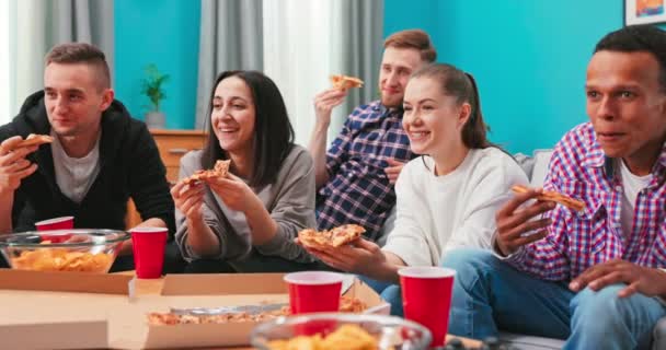 Felices amigos multiétnicos están comiendo pizza con queso, charlando relajante durante la fiesta de interior en el apartamento en — Vídeos de Stock