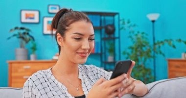 Memnun bir kadın oturma odasındaki kanepede oturuyor ve elinde telefonu var.