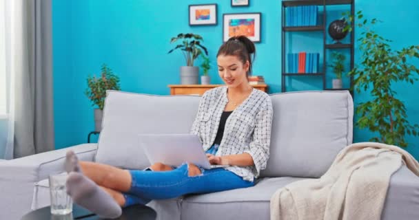 Ambitieuze student brengt de middag op de bank met laptop schrijven undergraduate paper voor de universiteit, houdt benen — Stockvideo