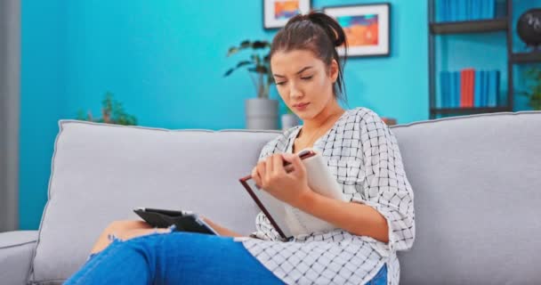 Mujer ocupada, pasa tiempo estudiando con la tableta y el libro, lee el libro de texto, comprueba las tareas resueltas, encuentra — Vídeo de stock