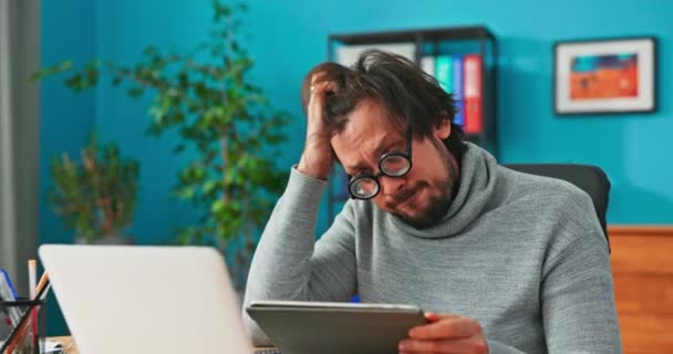 Tipo confundido, nuevo empleado de la empresa, está sentado en la oficina con gafas divertidas, sosteniendo un — Vídeos de Stock