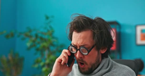 Hombre divertido con grandes gafas redondas negras, contesta el teléfono del cliente, hace bromas, no está bien informado, — Vídeos de Stock