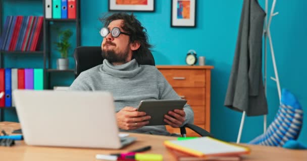 Funny empleado de la empresa se sienta en la silla con los pies en la mesa, con calcetines de colores, gafas redondas — Vídeo de stock