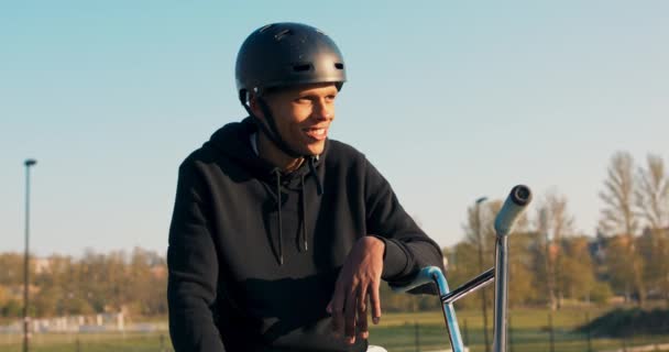 Молодий студент посміхається, коли він сидить зі своїм велосипедом на пандусі і — стокове відео