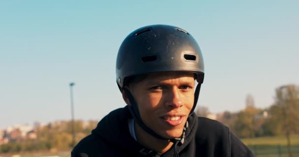 Un adolescent en sweat-shirt noir et casque se tient sur une rampe d'accès à un skatepark — Video