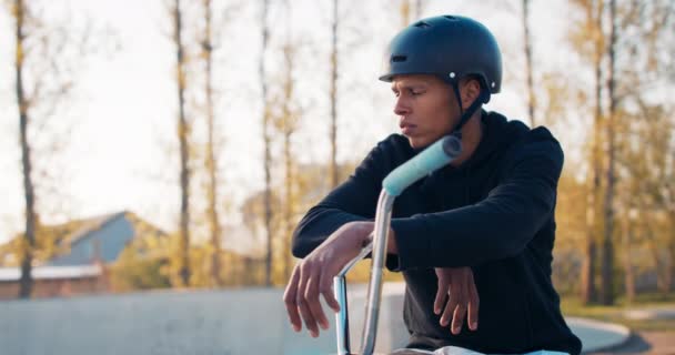 Un hombre de piel oscura con un casco de pie en un parque descansando después de un paseo en bicicleta, — Vídeos de Stock