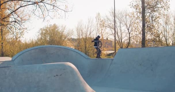 Profesional, truco, ciclista, adolescente vestido con ropa suelta, monta bmx por la rampa, pared inclinada, se cierne — Vídeo de stock