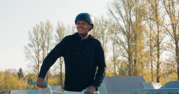 Stolt, selvsikker mørkhudet mand iført hjelm går gennem park ramper, ridning lav cykel ved siden af ham, – Stock-video