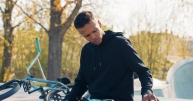 Bisikletten düşmüş bir bisikletçi, bir BMX, ve betonun üzerinde oturuyor.