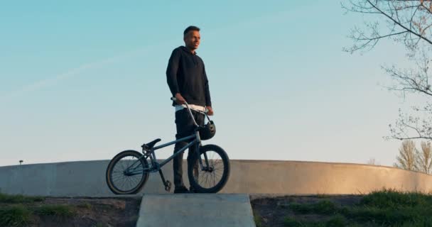 Bonito menino bmx em pé na rampa, segurando bicicleta e capacete na mão, vestido tudo em — Vídeo de Stock