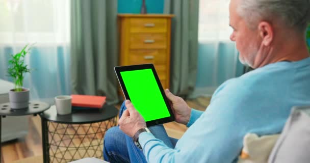 Oudere man thuis gebruikt Green Mock-up Screen Tablet. Hij zit op een bank. — Stockvideo