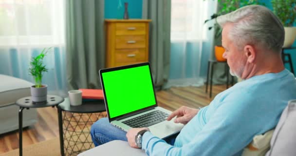 Senior Mann arbeitet an einem Laptop-Computer mit grünem Bildschirm, der auf einer Couch sitzt — Stockvideo